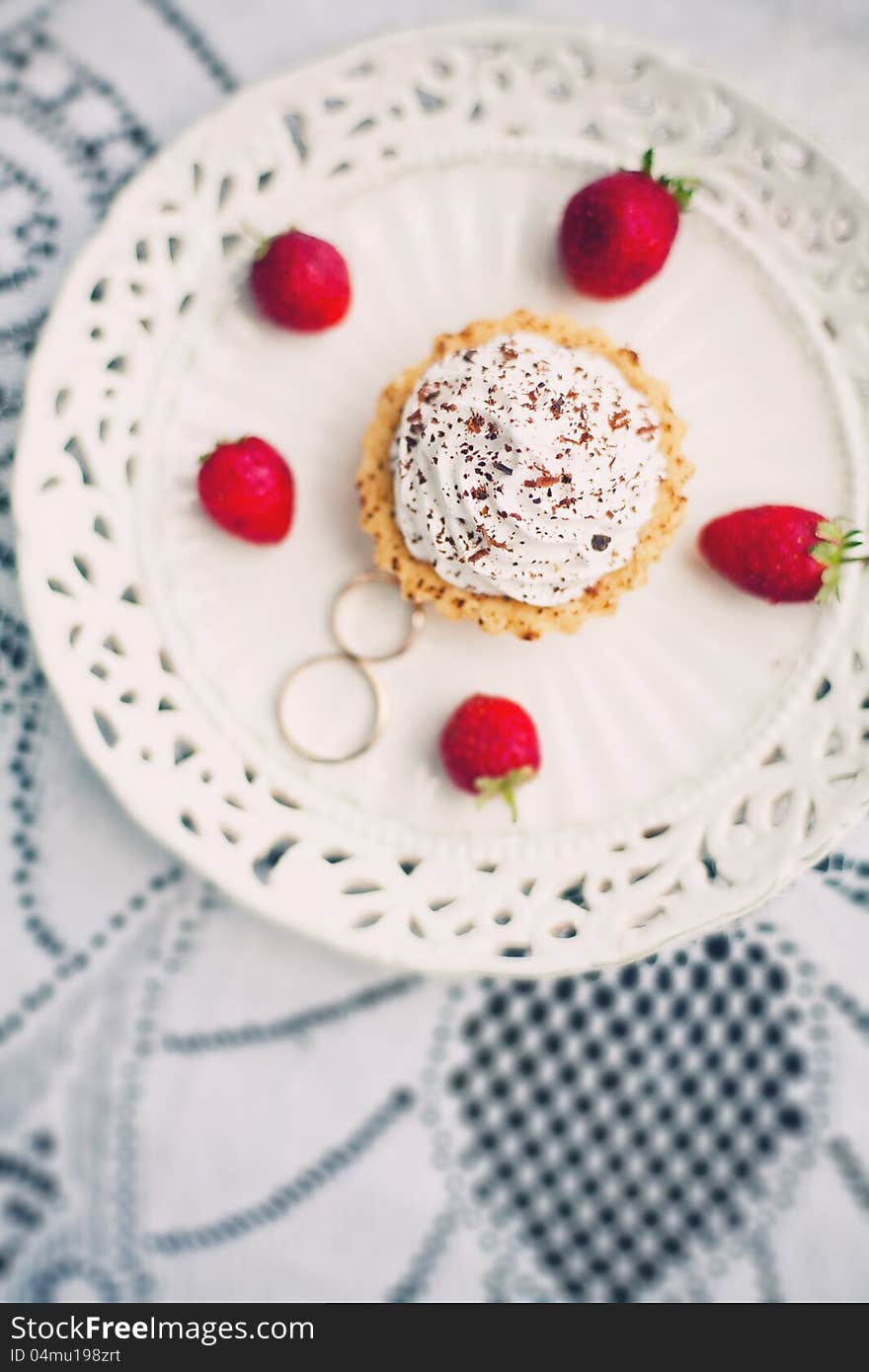 Wedding ring in the saucer with cake, strawberries and berries on a white lace tablecloth. Wedding ring in the saucer with cake, strawberries and berries on a white lace tablecloth