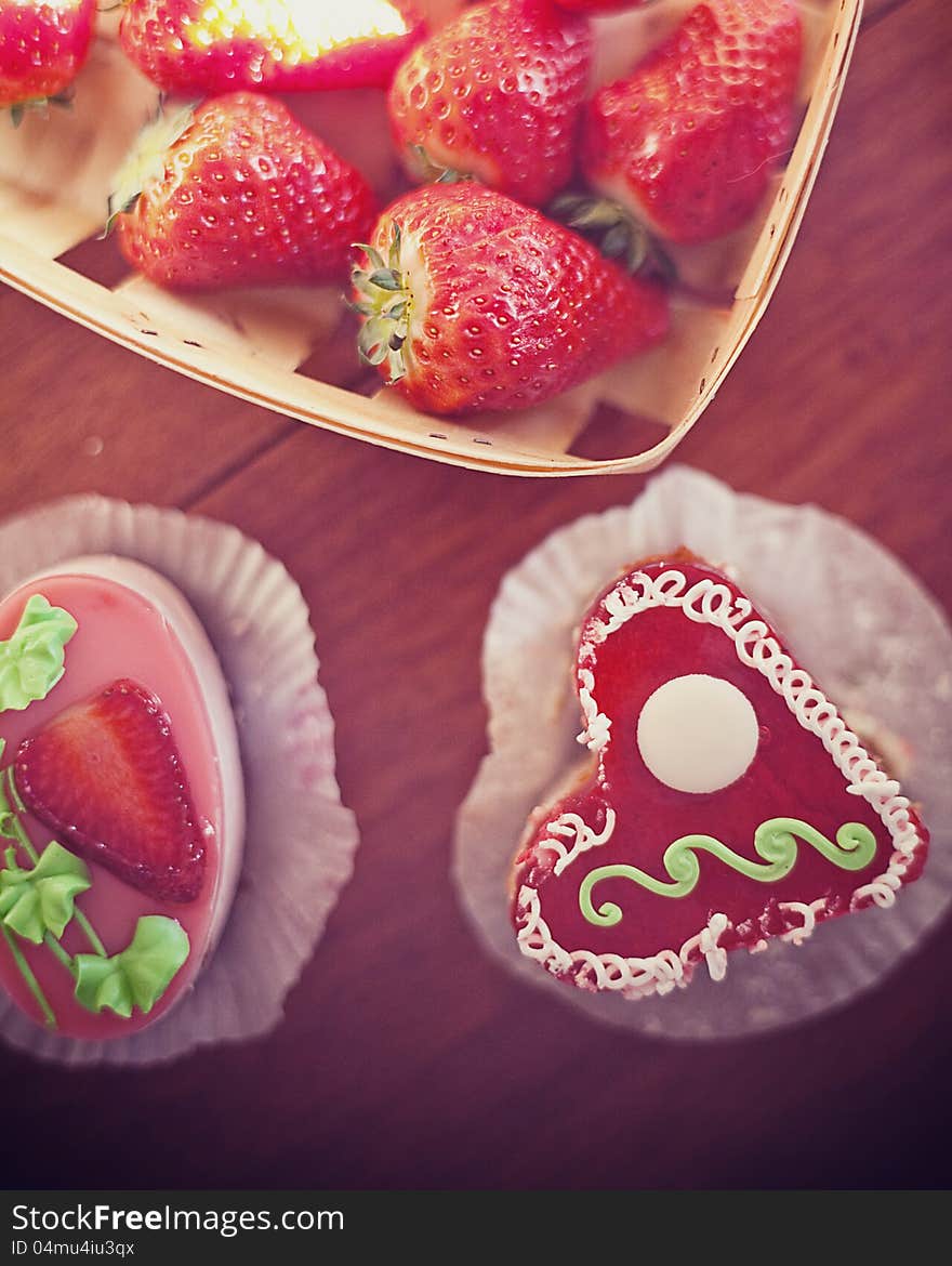 Strawberry cake in the shape of a heart,  near a basket of strawberries and another cake