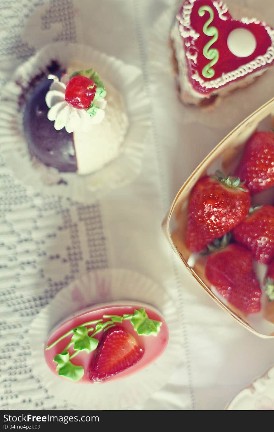 Strawberry cake in the shape of a heart,  near a basket of strawberries and another cake