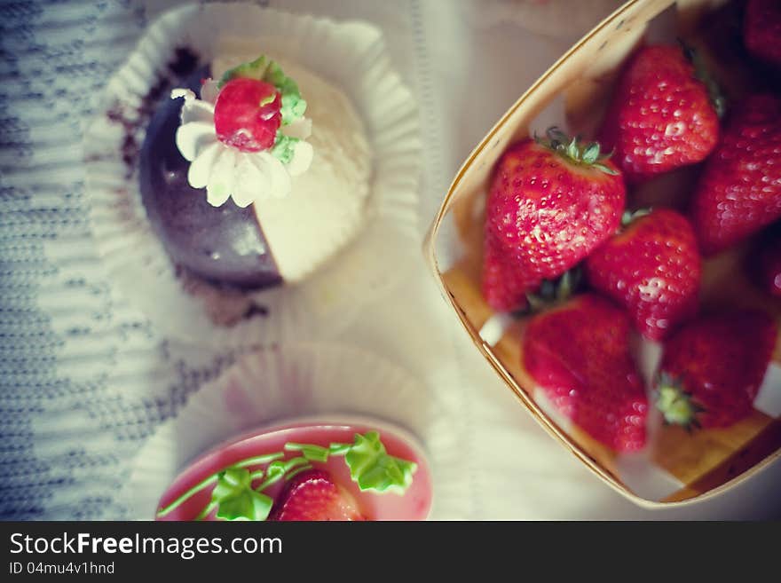 Strawberry cake in the shape of a heart,  near a basket of strawberries and another cake