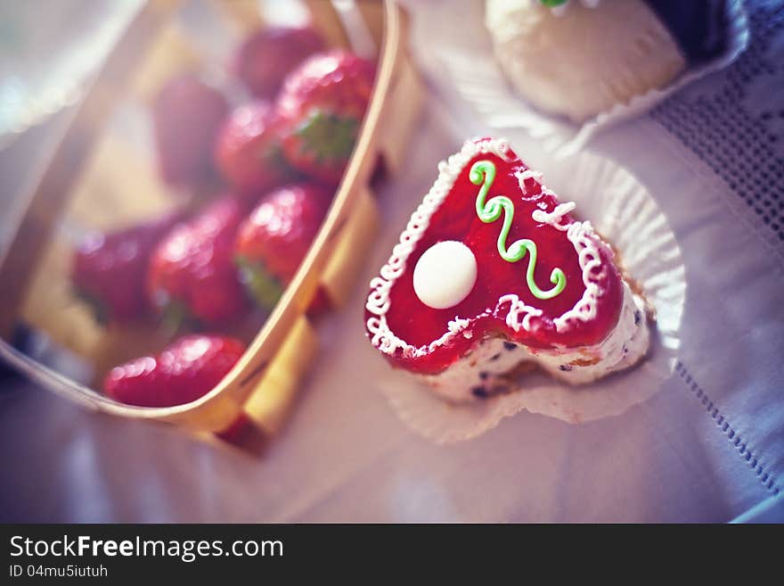 Strawberry cake in the shape of a heart,  near a basket of strawberries and another cake