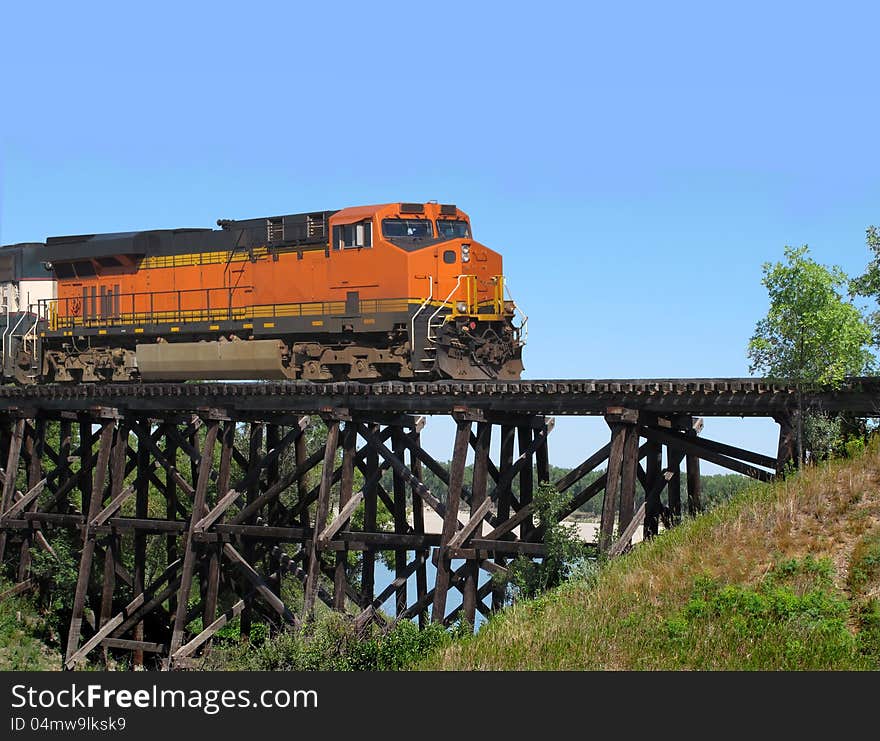 Railroad train locomotive crossing an old wooden trestle over a prairie coulee. Background of blue sky. Railroad train locomotive crossing an old wooden trestle over a prairie coulee. Background of blue sky.