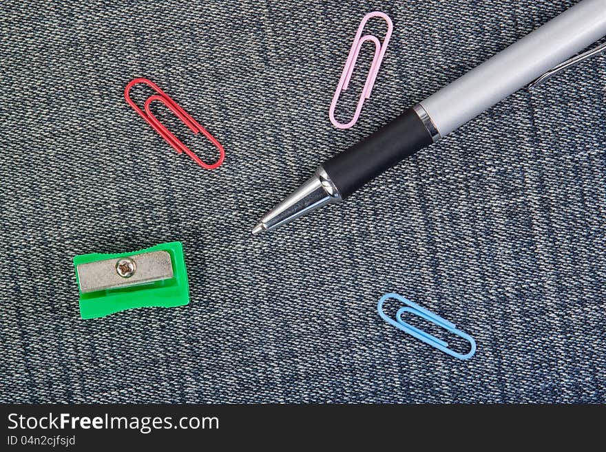 Pen, pencil sharpener and clip close-up on the background of denim material. Pen, pencil sharpener and clip close-up on the background of denim material.