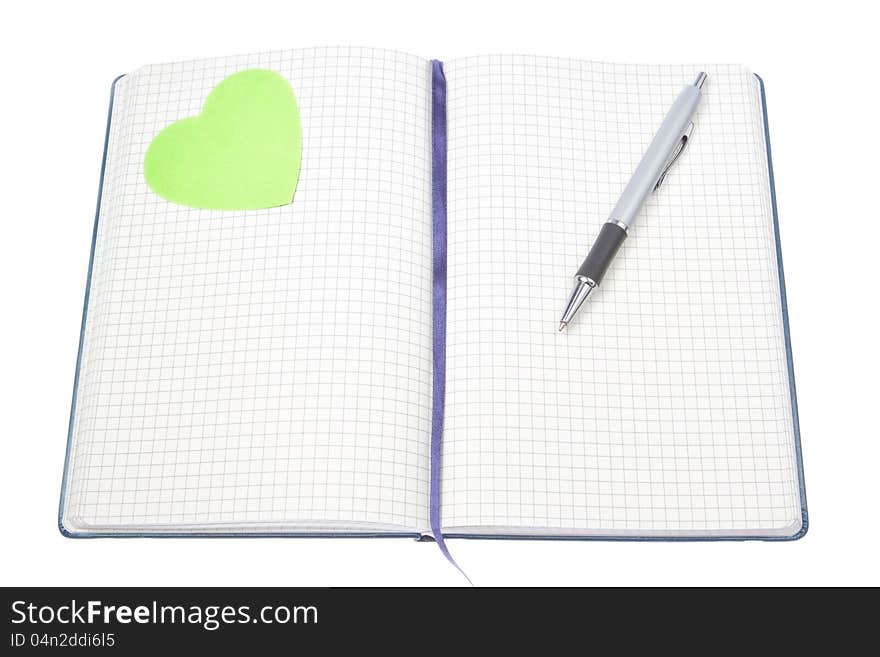 Open notepad with a pen and a green heart. Close-up.