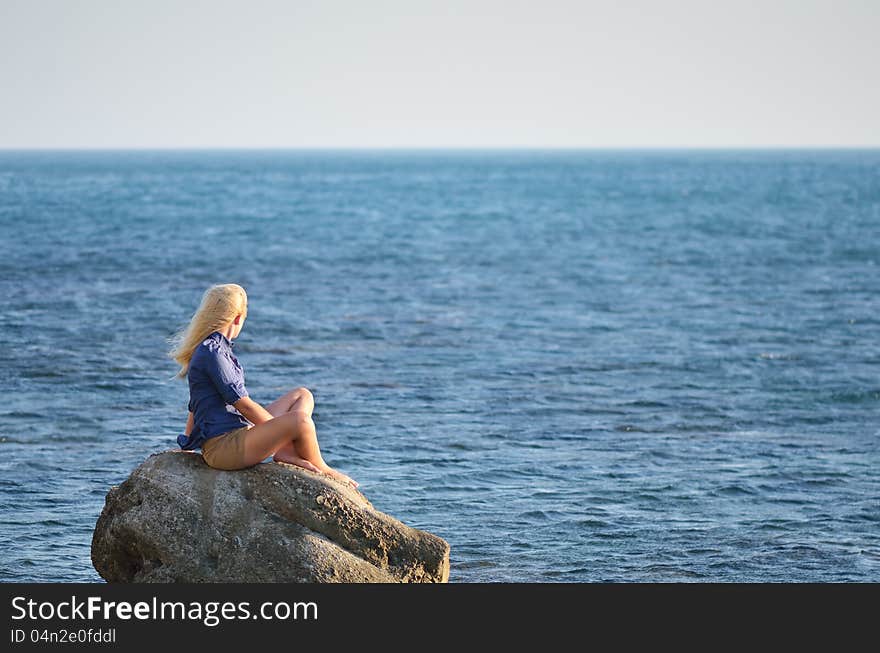Girl in the blue shirt sitting on a rock and looking at the sea. Girl in the blue shirt sitting on a rock and looking at the sea