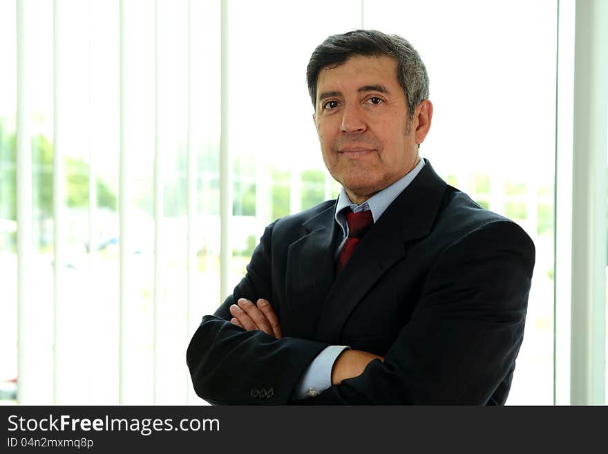 Mature Hispanic businessman with arms crossed inside an office building. Mature Hispanic businessman with arms crossed inside an office building