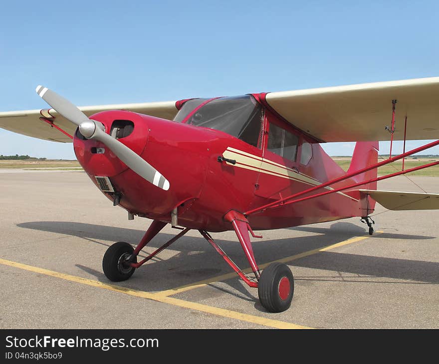 Close-up of the front part of an old small single engine red tail-wheel high-wing airplane sitting on the tarmac. Close-up of the front part of an old small single engine red tail-wheel high-wing airplane sitting on the tarmac.