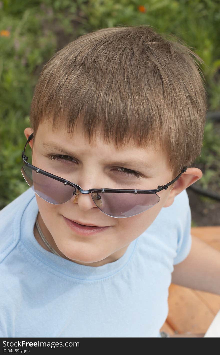 The boy (10 years) looks through sunglasses against a green lawn. The boy (10 years) looks through sunglasses against a green lawn