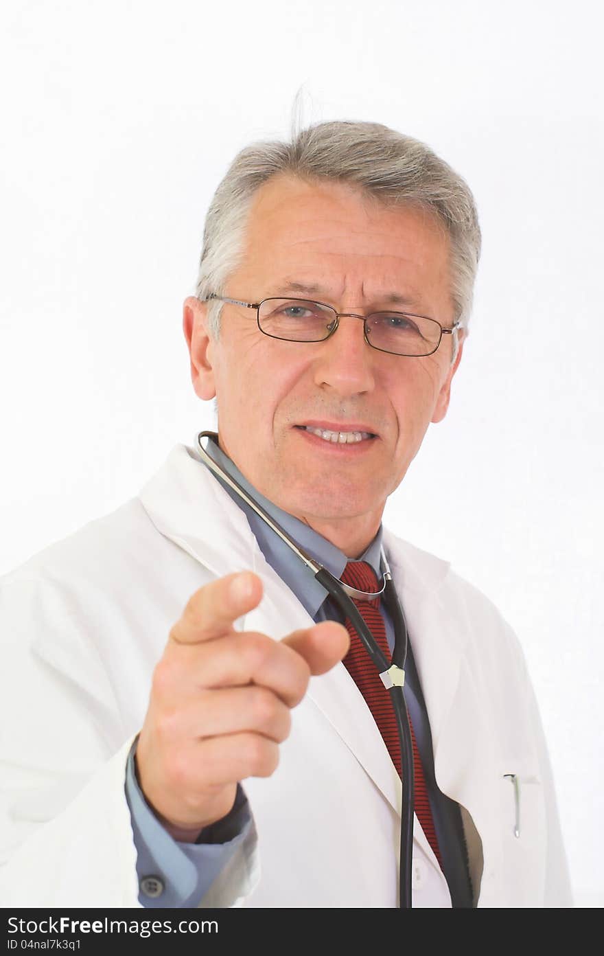 Vertical portrait of  matured, graying doctor with stethoscope on his neck. His eyes attendive but cheerful. He wears a physician’s white coat, a blue shirt an a red tie. His forefinger indicates the viewer. Vertical portrait of  matured, graying doctor with stethoscope on his neck. His eyes attendive but cheerful. He wears a physician’s white coat, a blue shirt an a red tie. His forefinger indicates the viewer