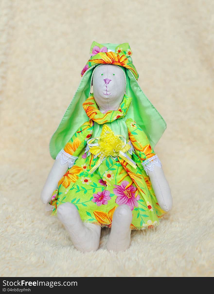 The doll a tilde hare in a green dress and a hat sits. The doll a tilde hare in a green dress and a hat sits