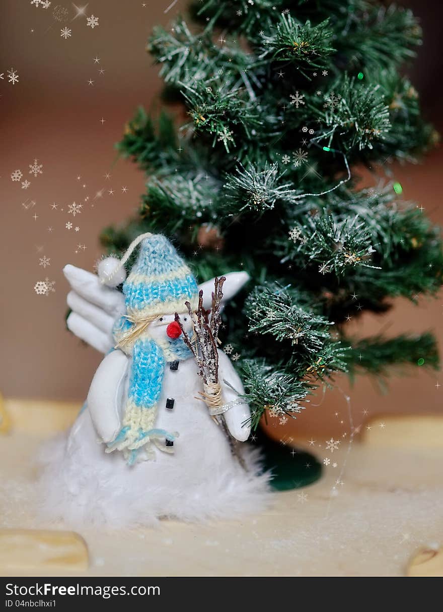 Toy angel a snowman in a blue cap under a fir-tree. Toy angel a snowman in a blue cap under a fir-tree
