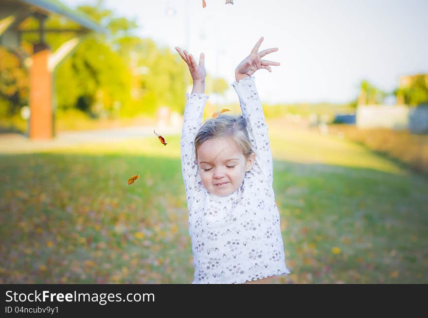 Pretty, young girl throwing leaves into the air while playing outside. Pretty, young girl throwing leaves into the air while playing outside.