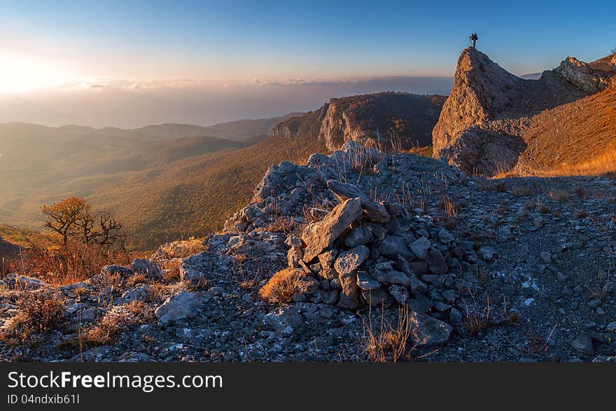 A man standing at mountain top with camera against a beautiful sunrise. A man standing at mountain top with camera against a beautiful sunrise