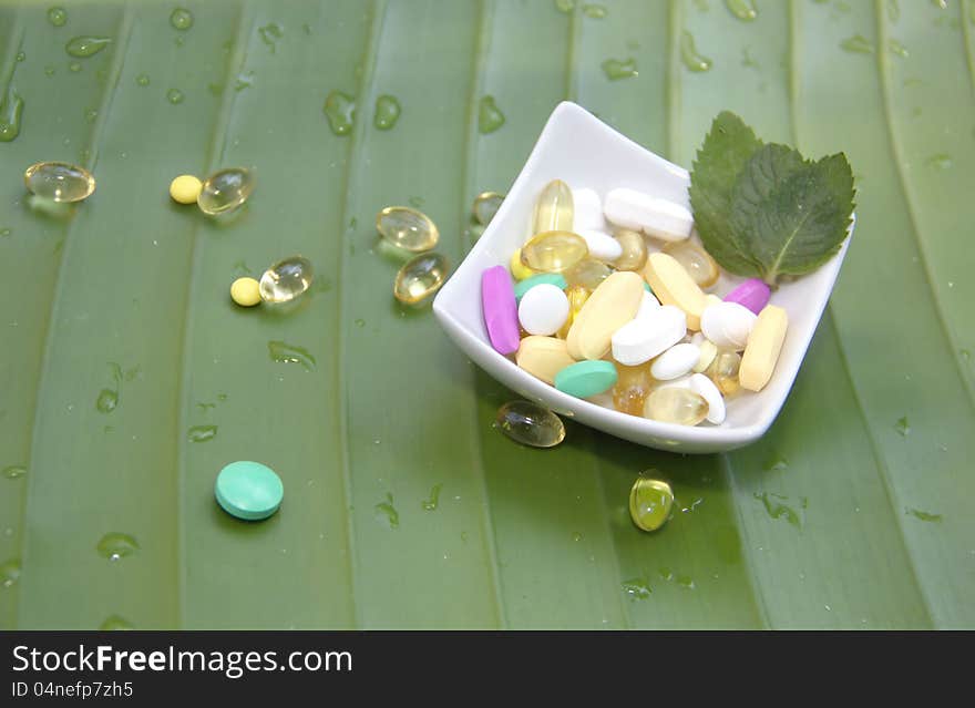 Assorted pills on green leaf background with drops of water. Assorted pills on green leaf background with drops of water