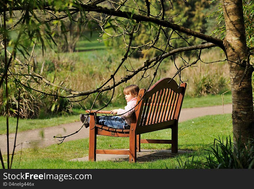 Little girl sitting on a bench in the park. Little girl sitting on a bench in the park