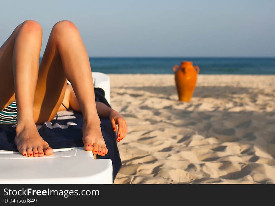 Legs of a beautiful woman relaxing on the beach with a amphora and the sea in the background. Legs of a beautiful woman relaxing on the beach with a amphora and the sea in the background