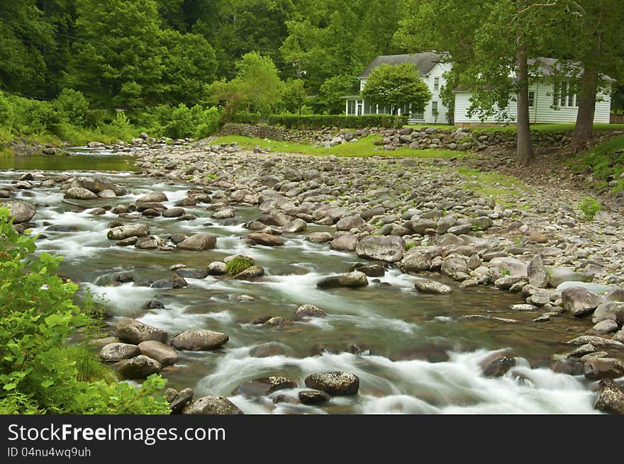 A white water stream flows by a white house. A white water stream flows by a white house.