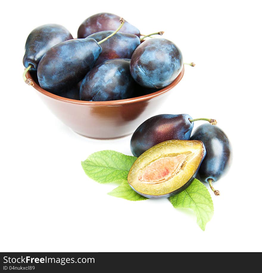 Bowl full of plums and  plus with green leaves   on a white background