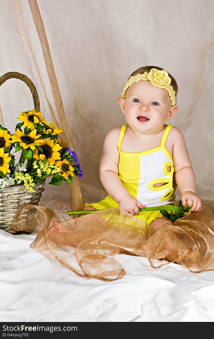 Baby girl sitting and smiling near the basket with flowers