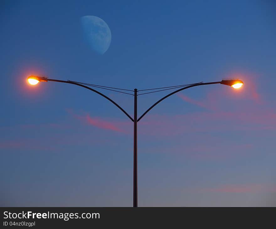 Streetlight glowing at the sunset with moon rising in the background. Streetlight glowing at the sunset with moon rising in the background