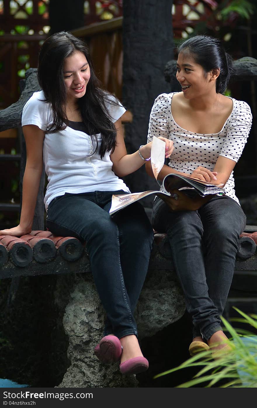 Pretty southeast asian girls doing activity outdoor. Reading and sharing information they found on a book/ magazine at outdoor scene. Pretty southeast asian girls doing activity outdoor. Reading and sharing information they found on a book/ magazine at outdoor scene