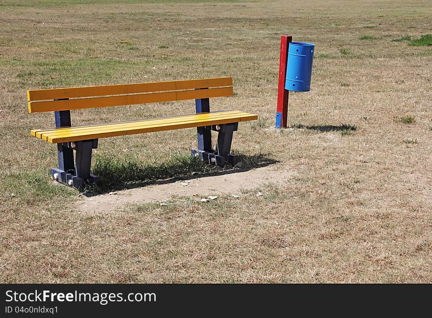 Yellow bench and blue recycle bin in the park