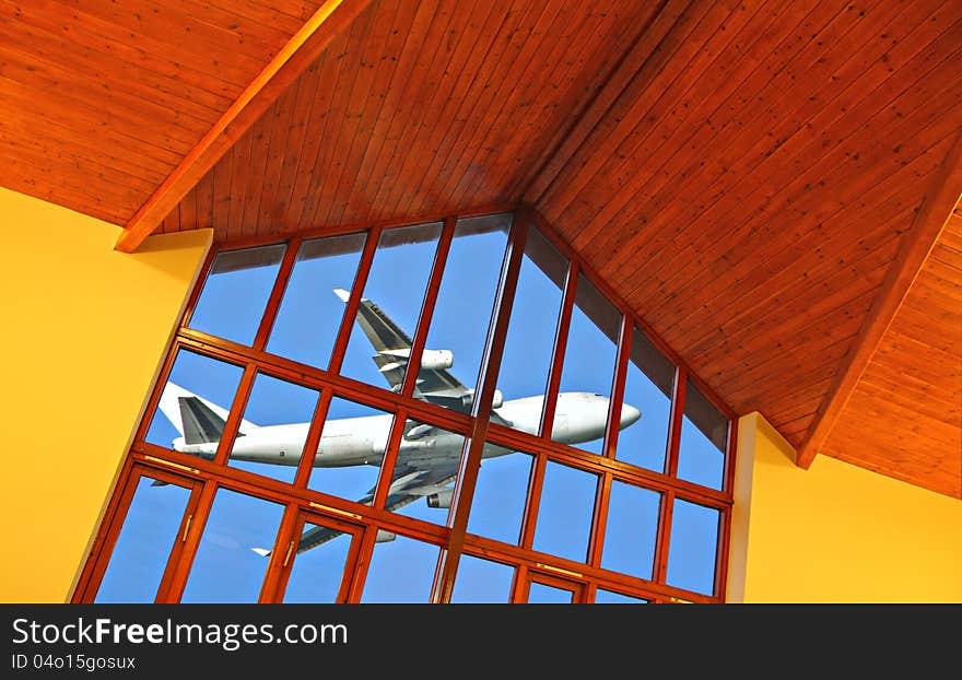 Photo of a modern international airport departure lounge showing plane through large aspect window.