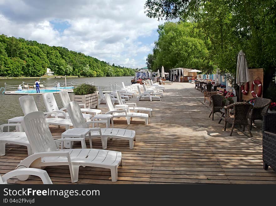 A Lounge chairs on a wooden pier on the river. A Lounge chairs on a wooden pier on the river