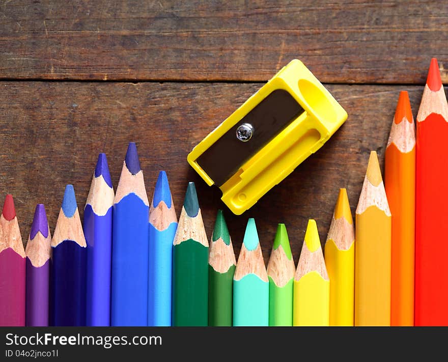 Closeup of variegated crayons in a row near pencil sharpener on wooden background