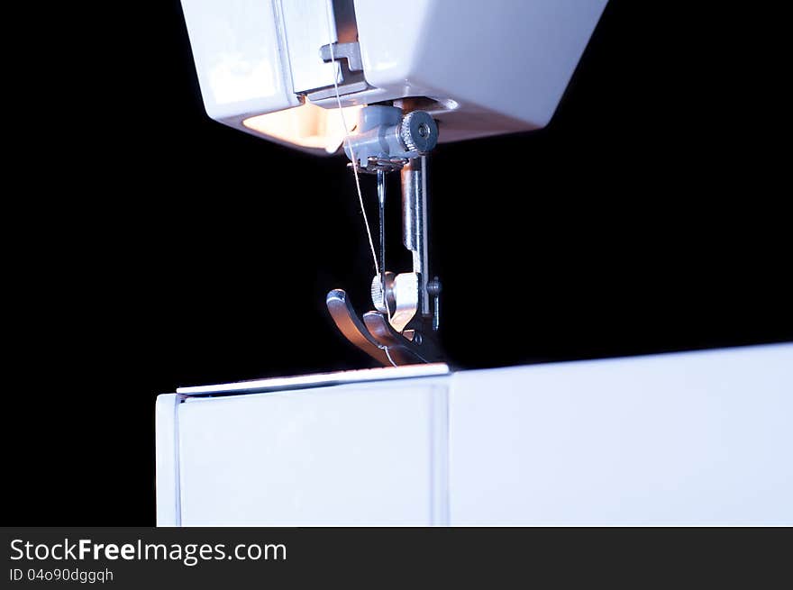 A needle with thread and foot of a sewing machine against a black background. A needle with thread and foot of a sewing machine against a black background