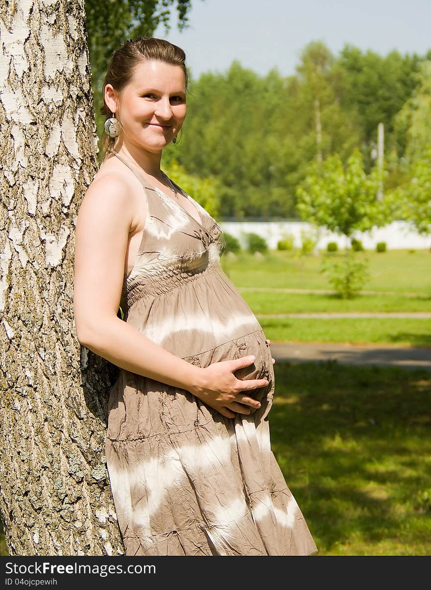 A pregnant girl is standing at the tree in nature