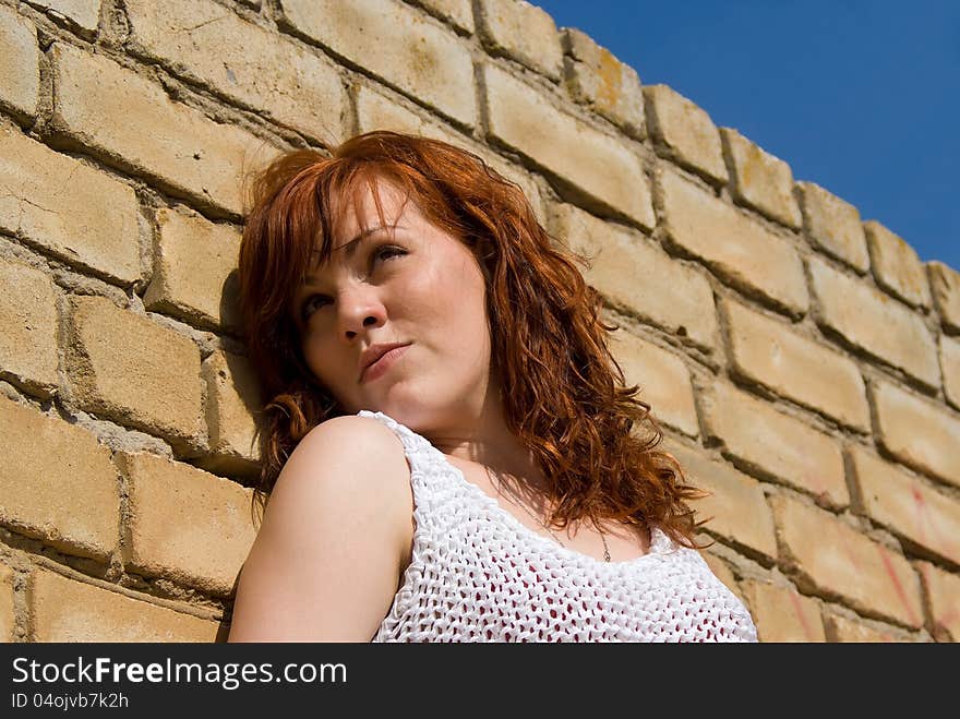 A beautiful red-haired girl standing by the wall