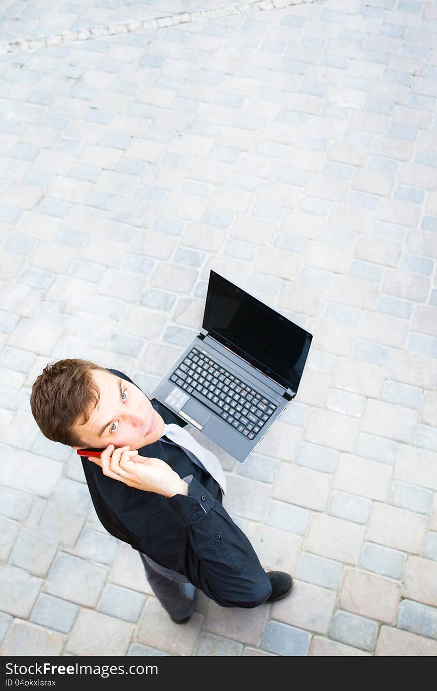 The image on top of a businessman standing in the street, which works with the computer and talks on a cell phone. The image on top of a businessman standing in the street, which works with the computer and talks on a cell phone.