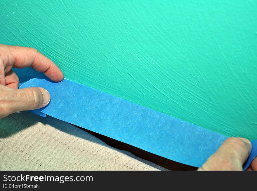 An image of a green wall being prepared for painting with blue painters tape