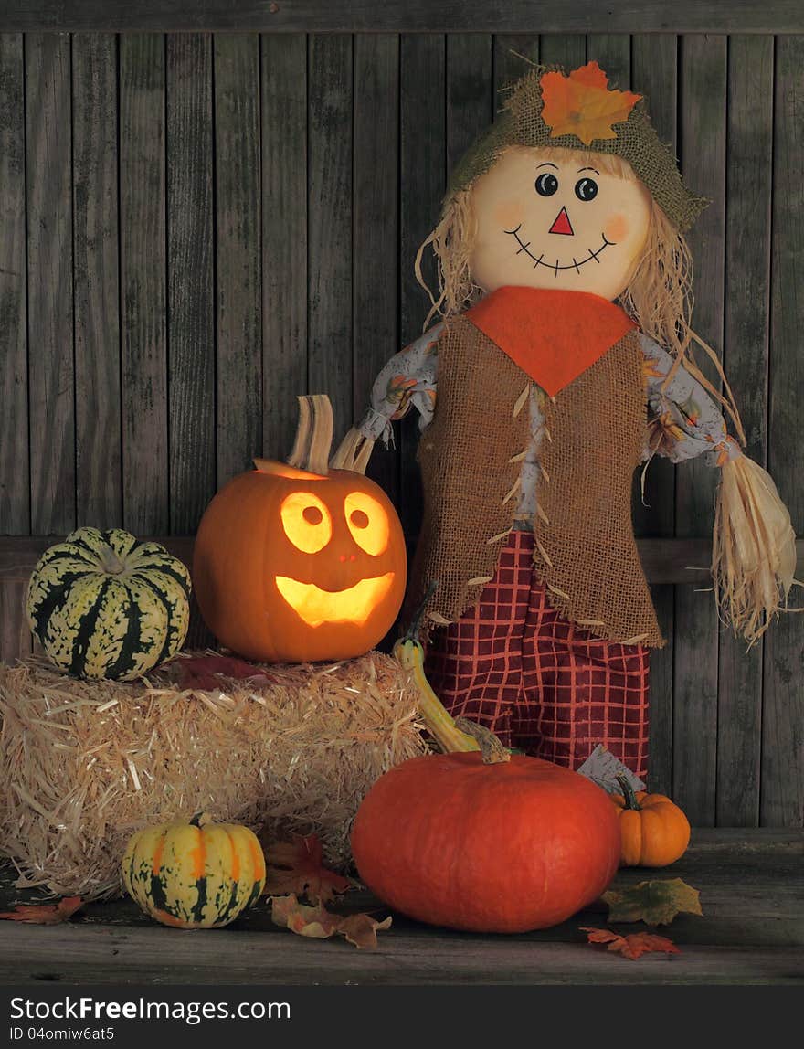 Smiling jack-o-lantern and straw doll with autumn squash