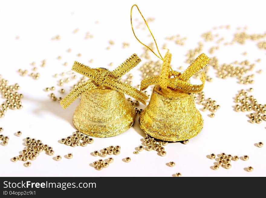 Against the background of golden beads scattered two Christmas Christmas gold bells with bows. Against the background of golden beads scattered two Christmas Christmas gold bells with bows