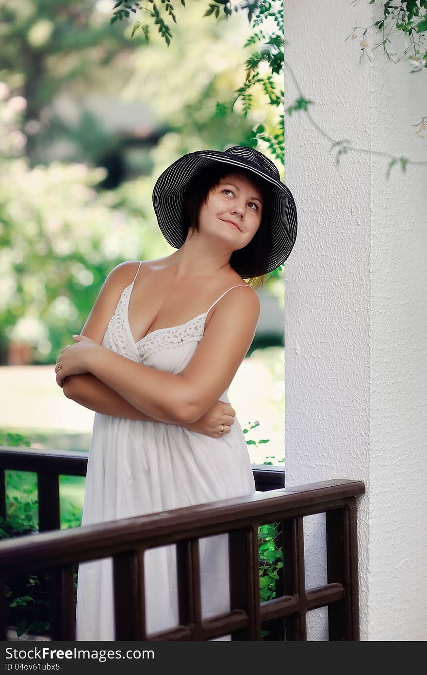 Girl in a white dress and black hat posing on the balcony. Girl in a white dress and black hat posing on the balcony