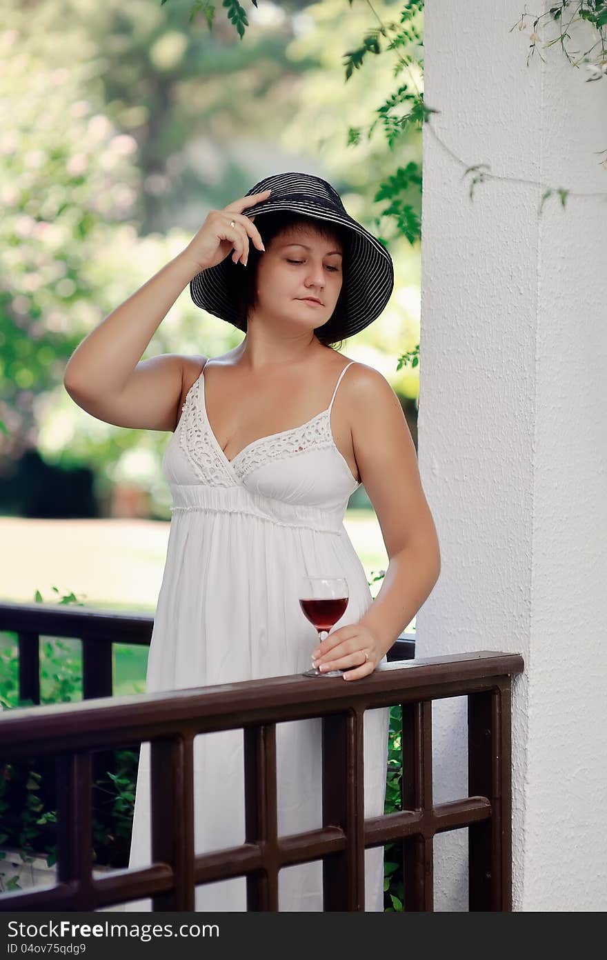 Posing girl in a white dress and a black hat with a wine glass. Posing girl in a white dress and a black hat with a wine glass