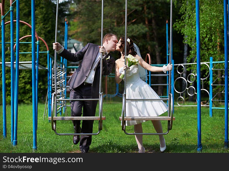 Romantic kiss bride and groom on swing in summer park