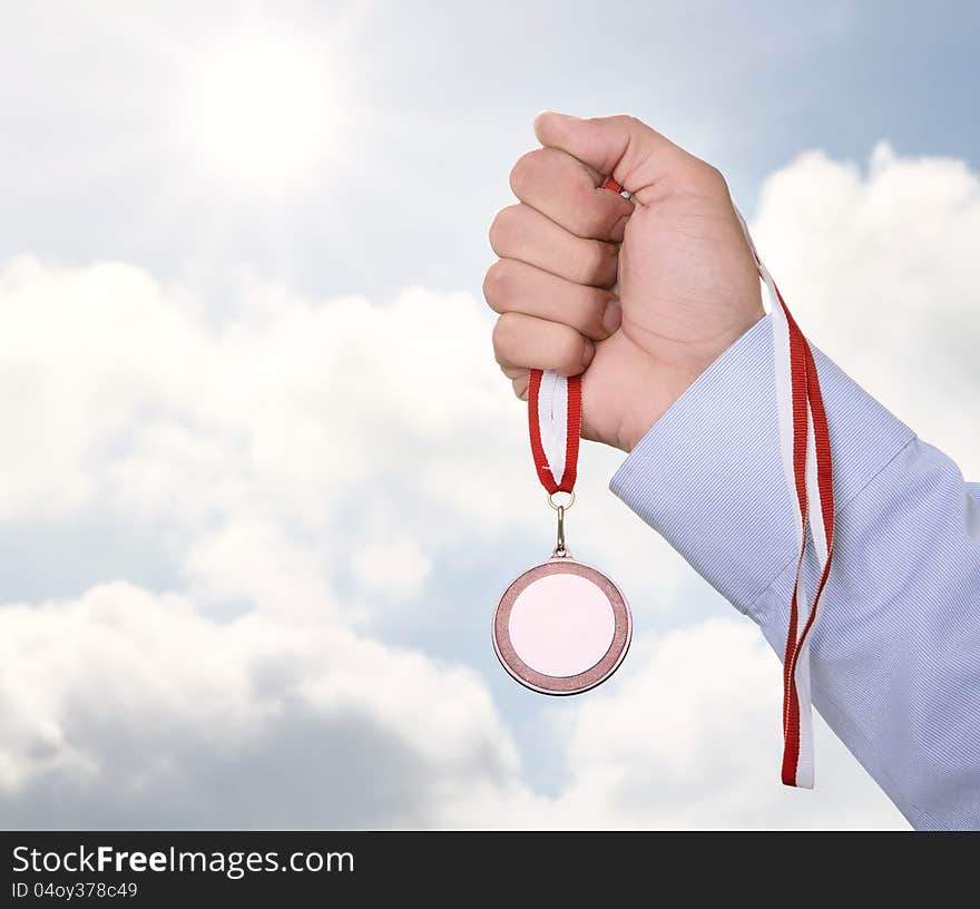 Businessman holding blank gold medal over cloudy sky with copy space. Businessman holding blank gold medal over cloudy sky with copy space
