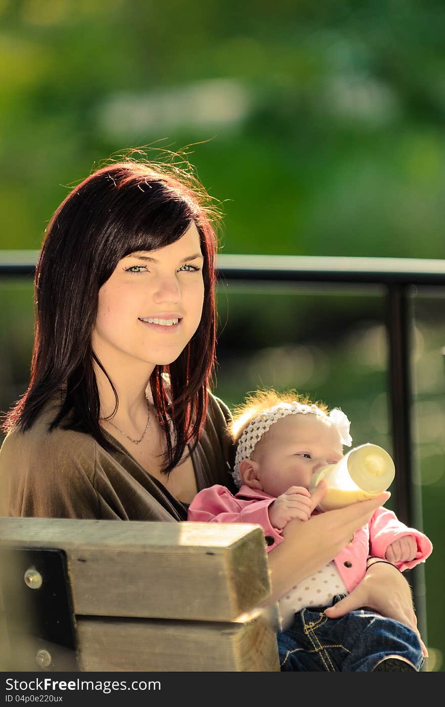 Young mother feeding her baby daughter in an outdoor park. Young mother feeding her baby daughter in an outdoor park.