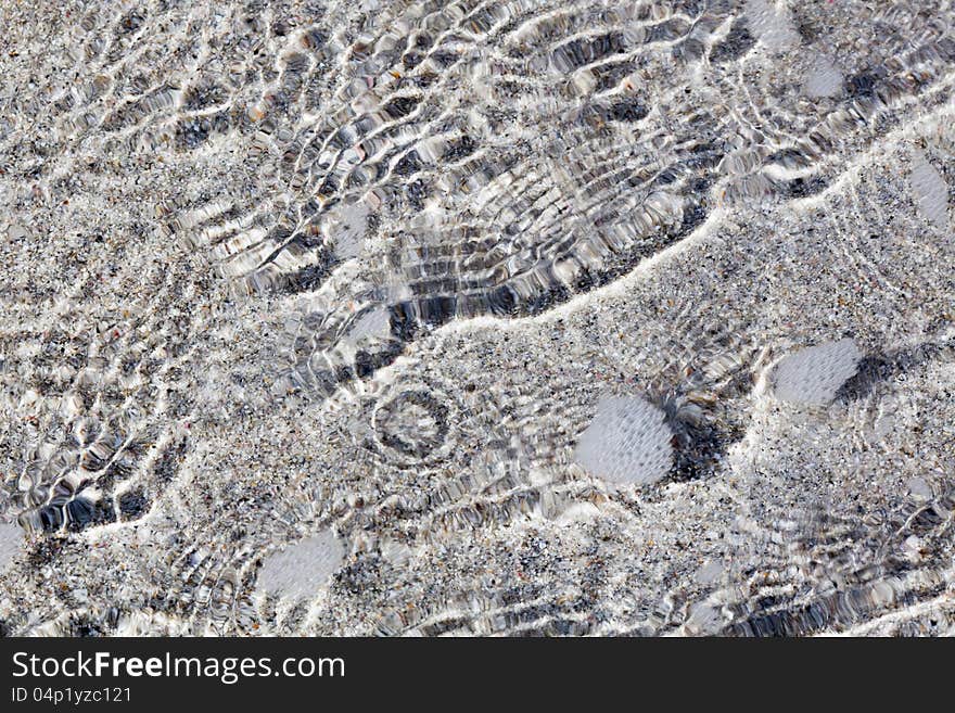 Background texture with water ripples at the seafront, with the sand of the beach shining through the flat water. Background texture with water ripples at the seafront, with the sand of the beach shining through the flat water