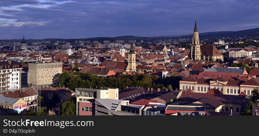 A panoramic view of Cluj Napoca, Transylvania, with its churches, at dusk, under a clouded sky. Viewed from the Citadel Hill.