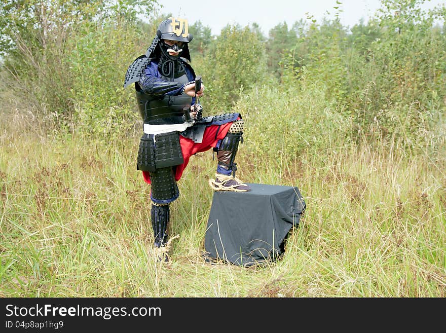 Man dressed in Japanese armor of the XVI century booted in straw sandals (varaji) pulling out his sword. Man dressed in Japanese armor of the XVI century booted in straw sandals (varaji) pulling out his sword