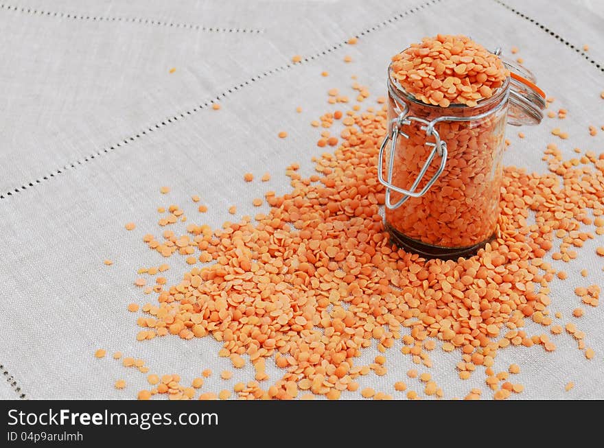 Red lentils spilled out from jar on grey linen table napkin. Red lentils spilled out from jar on grey linen table napkin