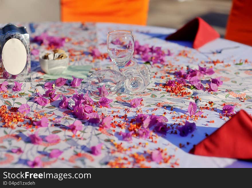 On the table and scattered flower petals are red wine glasses and napkins. On the table and scattered flower petals are red wine glasses and napkins