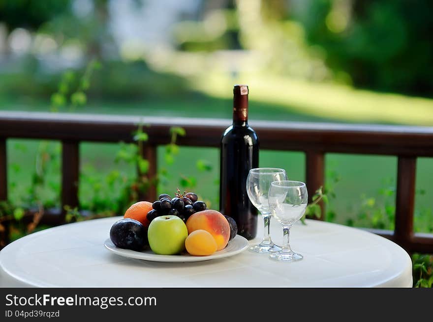 On the white table is a bottle of wine with glasses and ripe fruit. On the white table is a bottle of wine with glasses and ripe fruit