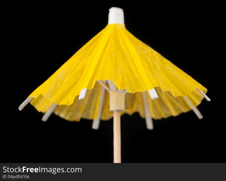 A bright yellow cocktail umbrella with a toothpick on black background. A bright yellow cocktail umbrella with a toothpick on black background