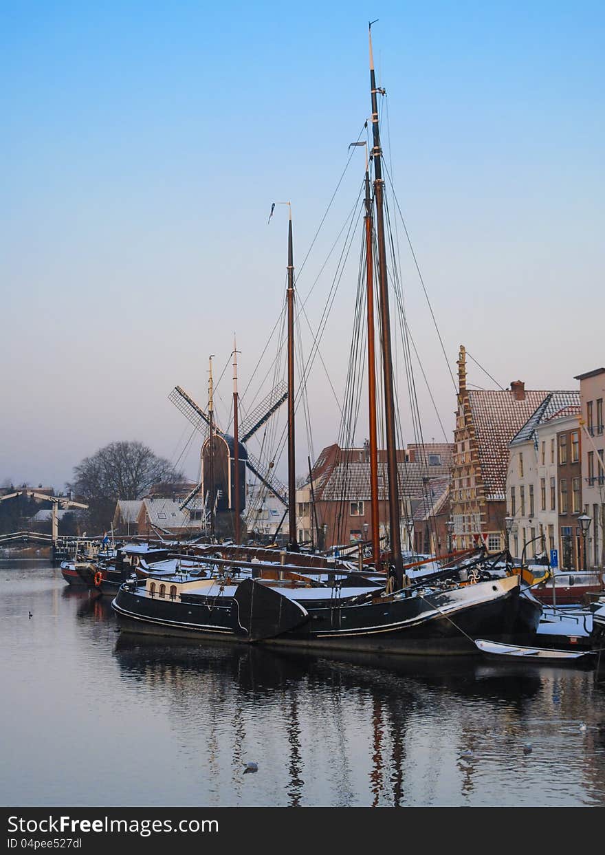 View of winter Amsterdam with old historical building, canal, boats and windmill