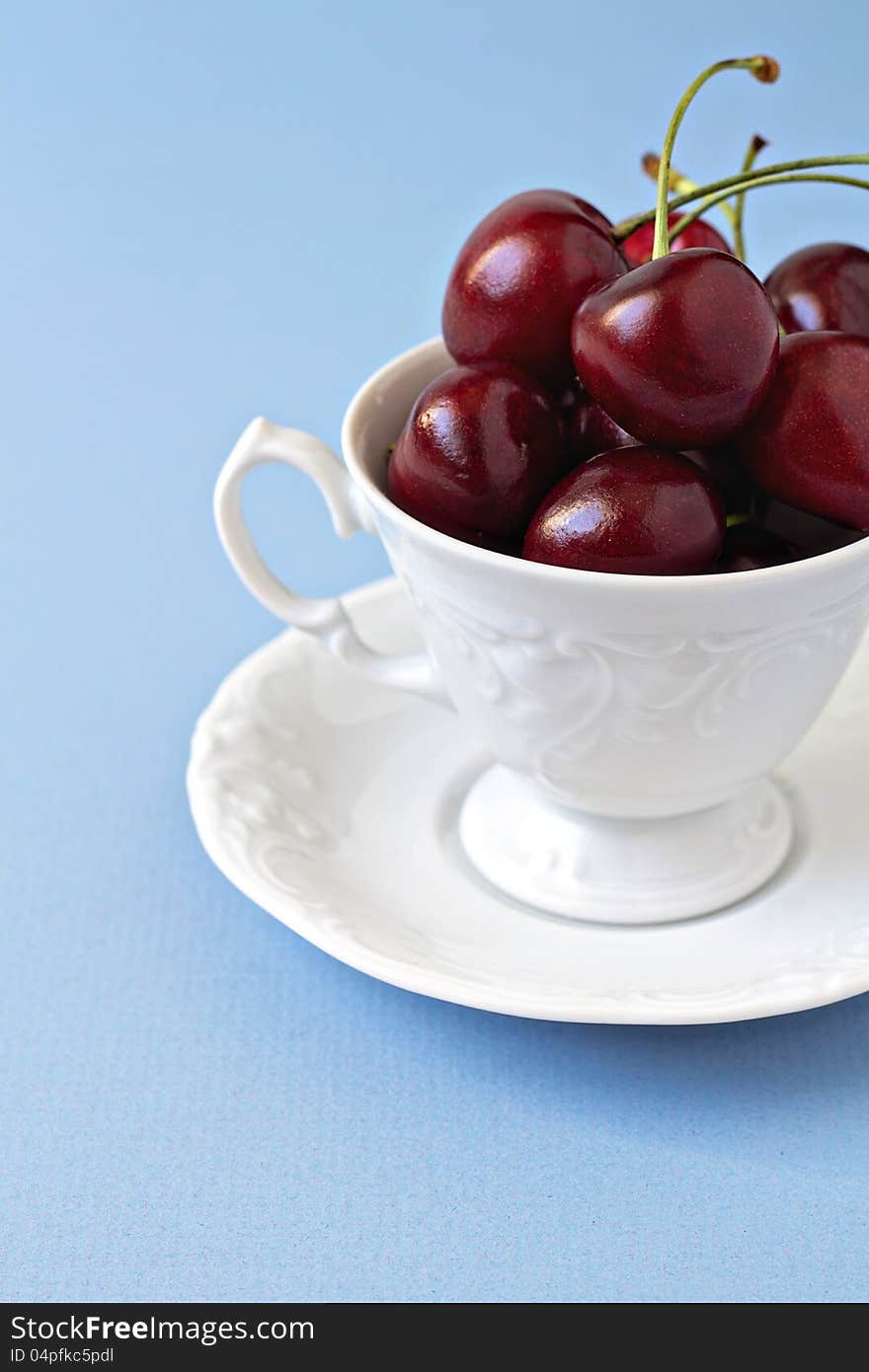 Sweet cherries in a white cup on a light blue background